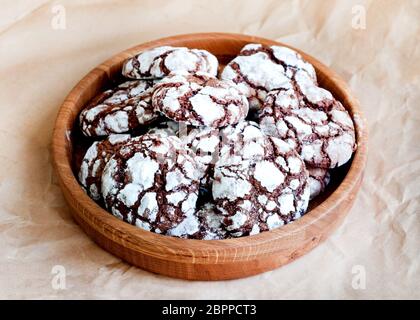 Biscotti al cioccolato fessurati cosparsi di zucchero a velo in un piatto di legno. Biscotti natalizi al cioccolato. Foto Stock