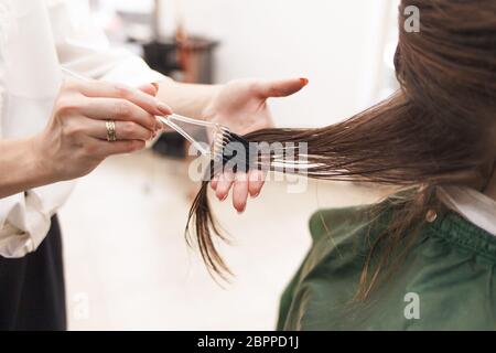 Il parrucchiere applica una maschera per capelli alla donna nel salone di bellezza. Procedura di raddrizzatura dei capelli con Botox e cheratina Foto Stock