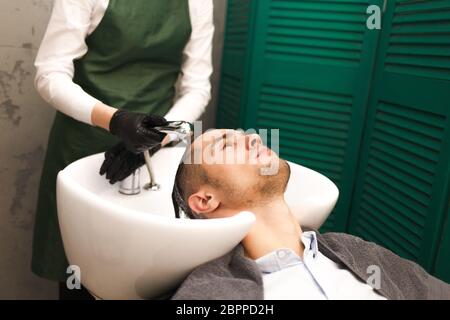 Il parrucchiere lava i capelli del cliente prima di tagliarli. Un uomo serio e bello lava la testa in un salone di bellezza Foto Stock