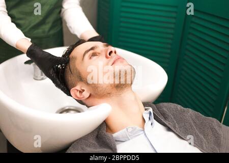 Il parrucchiere lava i capelli del cliente prima di tagliarli. Un uomo serio e bello lava la testa in un salone di bellezza Foto Stock