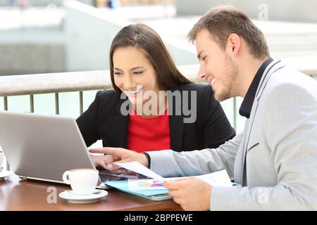 Due dirigenti che lavorano in linea con un computer portatile seduto in una terrazza bar Foto Stock