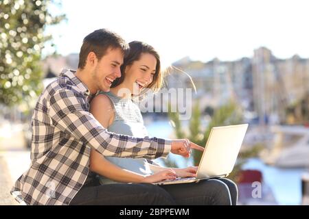 Coppia felice utilizza un laptop seduto in una porta su vacanze estive Foto Stock