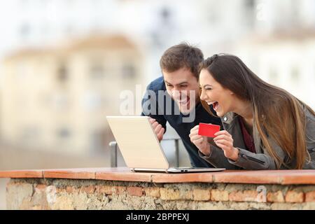 Entusiasti acquirenti online per trovare le offerte su un computer portatile in un balcone in vacanza Foto Stock