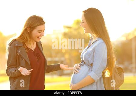 Stupito riunione donna incinta amico in un parco al tramonto Foto Stock