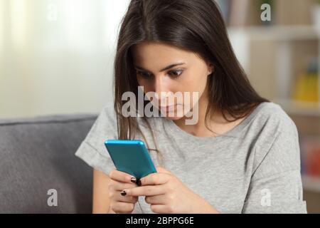 Ragazza texting ossessionato con uno smart phone seduta su un divano nel salotto di casa Foto Stock