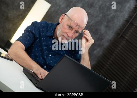 Un imprenditore senior utilizzando laptop, egli sta avendo difficoltà e problemi di visione Foto Stock