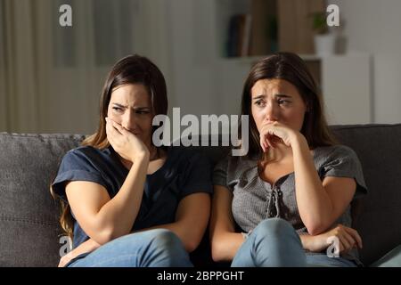 Vista frontale di due amici triste nel buio seduto su un divano nel salotto di casa Foto Stock