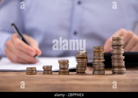 Close-up di un imprenditore il calcolo fattura utilizzando la calcolatrice nella parte anteriore di una pila di monete Foto Stock