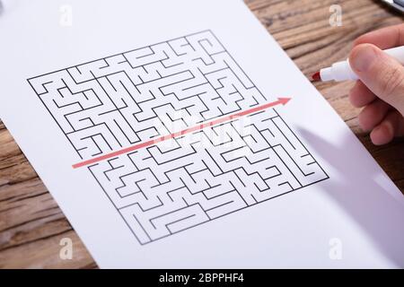 Close-up di persona la mano risolvendo puzzle labirinto con contrassegno rosso sulla scrivania in legno Foto Stock