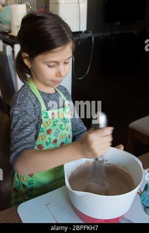 La ragazza produce una torta di crema al cioccolato, montando gli ingredienti in un recipiente grande Foto Stock