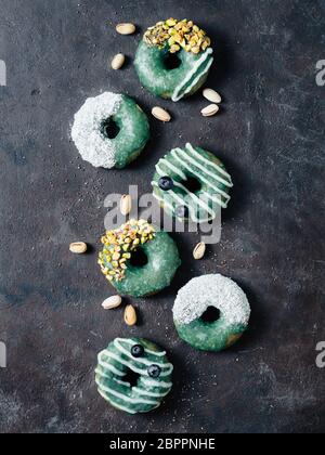 Vegan ciambelle con semi di Chia e rabboccato con sani spirulina smalto con pistacchio, noce di cocco essicata e mirtillo. Blu Verde spirulina ciambelle, su Foto Stock