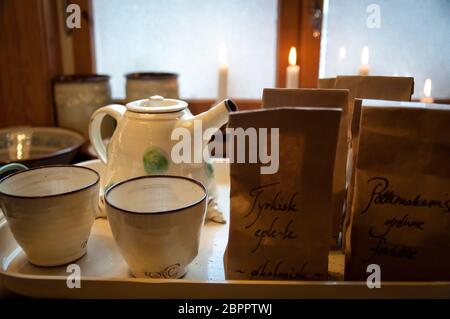 Accogliente serve il vassoio con ceramica teacups, teiera, tè e candele di fronte alla finestra - carta marrone bustine di tè con il testo turco apple organico e tè Foto Stock