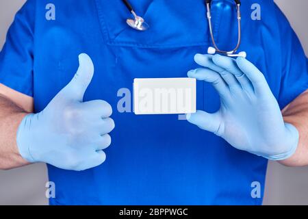 Medico di sesso maschile di indossare guanti in lattice blu è in possesso di una casella vuota white paper business card, close up Foto Stock