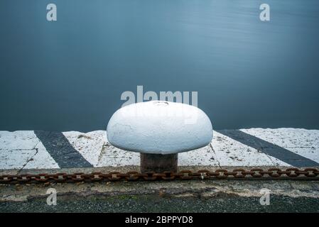 Tollard dipinto di colore bianco fresco sul molo del porto di Saint Malo. Una catena arrugginita corre da parte. Scatto a lunga esposizione. Foto Stock