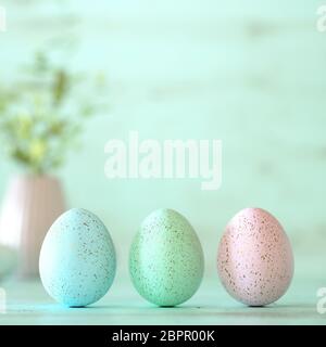 Tre pastello colorato le uova di Pasqua decorate con spruzzi d'oro, i fiori e le macchie di colore blu, verde e giallo su verde menta sullo sfondo di legno con copia Foto Stock