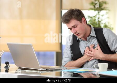 Imprenditore subisce un attacco di cuore con le sue mani afferrando il petto seduto in un desktop in ufficio Foto Stock