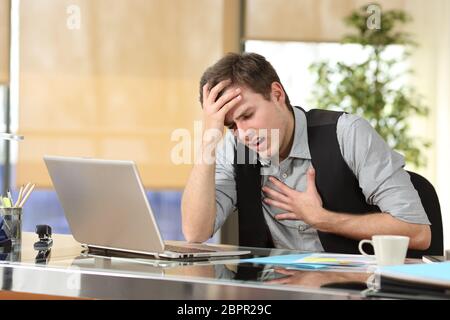 Imprenditore di subire un attacco di ansia con le mani nel suo petto e testa seduto in un desktop in ufficio Foto Stock