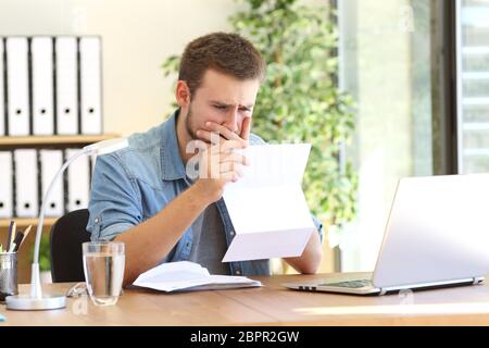 Preoccupati di imprenditore lavora e la lettura di una lettera con la cattiva notizia in una scrivania in ufficio Foto Stock