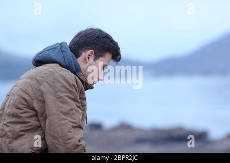 Vista laterale ortrait di un triste uomo in inverno sulla spiaggia lamenta Foto Stock