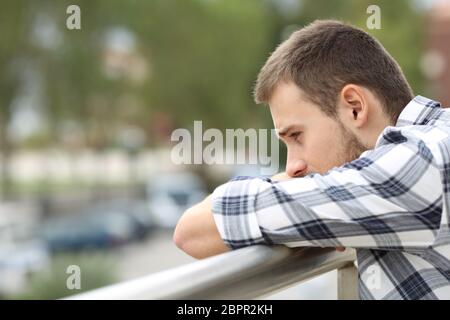 Vista laterale verticale di un triste singolo uomo guardando in giù da un balcone di una casa con un background urbano Foto Stock