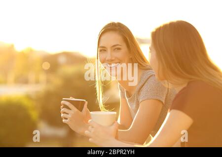 Due amici felici che parlano all'esterno in un balcone della casa al tramonto Foto Stock