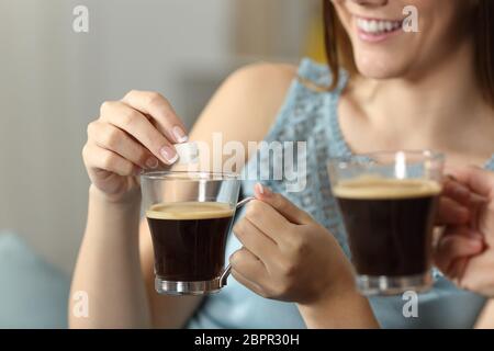 In prossimità di una donna mani gettando lo zucchero in una tazza di caffè seduto su un divano nel salotto di casa Foto Stock