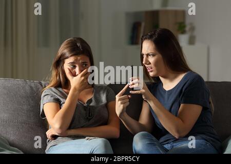 Arrabbiato donna scolding il suo amico circa il contenuto del telefono seduta su un divano nel salotto di casa Foto Stock