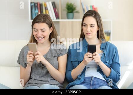 Invidioso donna guardando il suo amico gli sms in un telefono seduta su un divano nel salotto di casa Foto Stock