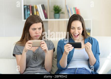 Vista frontale ritratto di un perdente invidiosi ragazza guardando il suo vincitore amico seduto su un divano nel salotto di casa Foto Stock