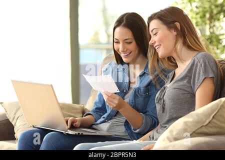 Due compagni di stanza di controllo mail banca on line con un laptop seduto su un divano nel salotto di casa Foto Stock