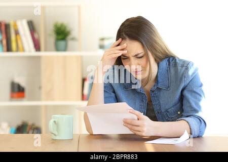 Preoccupato della donna la lettura di cattive notizie in una lettera su un tavolo a casa Foto Stock