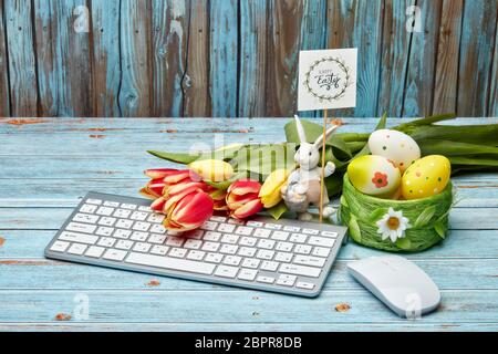 Uova di pasqua colorate, coniglio di pasqua, fiori di primavera, tastiera e mouse su sfondo di legno. Biglietto d'auguri, sfondo di Pasqua Foto Stock