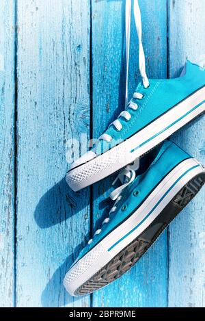 Coppia di blu sneakers tessile appesi ad un chiodo sulla parete del vecchio incrinato doghe in legno Foto Stock