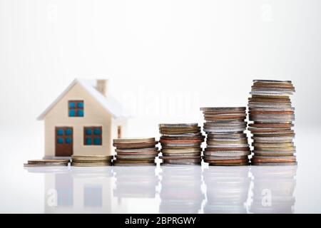 Aumentando le monete disposto nella parte anteriore del modello di casa sulla scrivania bianca Foto Stock