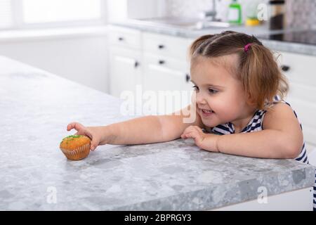 Sorridente ragazza carina la mano raggiungendo per la tortina sul banco di cucina Foto Stock