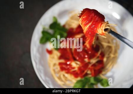 Gustosa e appetitosa pasta italiana di spaghetti con salsa di pomodoro, parmigiano e basilico su piatto su tavola scura Foto Stock