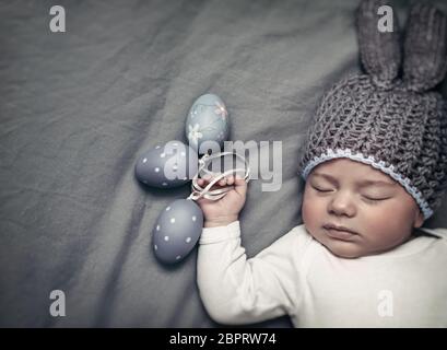 Closeup ritratto di un piccolo grazioso baby boy indossando il costume bunny e dormire con le uova decorative in mani su sfondo grigio, foto con copia spazio, Foto Stock