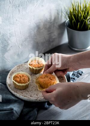 Muffin fatti in casa sulla piastra di artigianato grigio su un tavolo di legno. Tenere le mani tortina di carota. Copia dello spazio. Immagine dai toni in stile scandinavo. Foto Stock