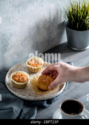 Muffin fatti in casa sulla piastra di artigianato grigio su un tavolo di legno. Tenere in mano la carota tortina. Copia dello spazio. Immagine dai toni in stile scandinavo. Foto Stock