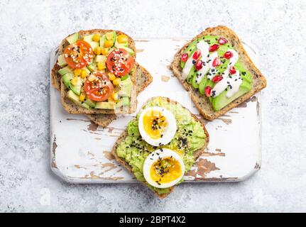 Toast di avocado con uova, pomodori, condimenti su legno bianco rustico tagliere su sfondo di pietra. Preparare dei sani panini all'avocado per la colazione Foto Stock