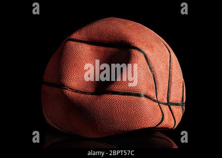 Sgonfiato e rompito vecchia palla da basket. Sfondo nero. Riflessione. Foto Stock