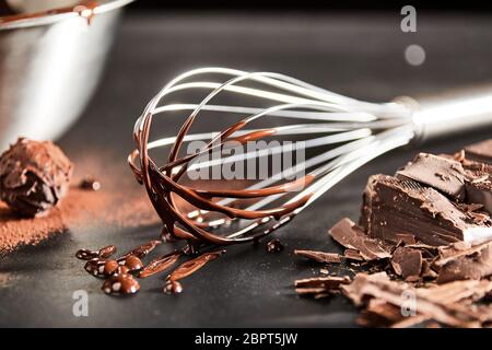 Il gocciolamento cioccolato fuso su un vecchio vintage frusta a fianco di un round bonbon o cookie e il trito di barretta di cioccolato Foto Stock