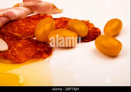 Un uovo di pollo spezzato senza guscio, fette di salsiccia e pancetta e pomodori su fondo bianco. Primo piano Foto Stock