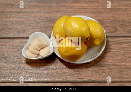 quattro limoni con compresse di vitamina c arancio in diversi piatti su un tavolo di legno vista dall'alto Foto Stock