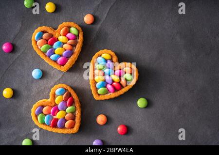 Colorati pulsanti Candy sulla torta a forma di cuore su ardesia sfondo nero - idea di compleanno Backgroundndy pulsanti sulla torta a forma di cuore su ardesia nera Bac Foto Stock