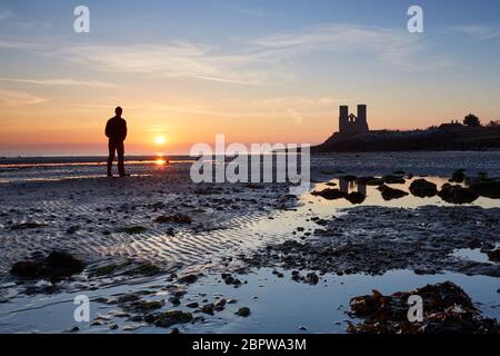 Reculver, Kent, Regno Unito. 20th maggio 2020: Tempo britannico. Un uomo guarda l'alba a Reculver Towers come la marea recede su ciò che si prevede di essere uno dei giorni più caldi dell'anno finora. Foto Stock