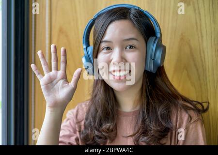 Asian giovane donna che sventola la mano per dire ciao quando fa la videochiamata ad un amico con la presa sociale, sorridente femmina che prende video blog che registra vlog, Foto Stock