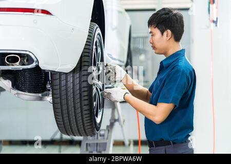 Meccanico asiatico controllo e riparazione delle ruote dell'auto nel centro di assistenza manutenzione che fa parte dello showroom, tecnico o tecnico professionista w Foto Stock