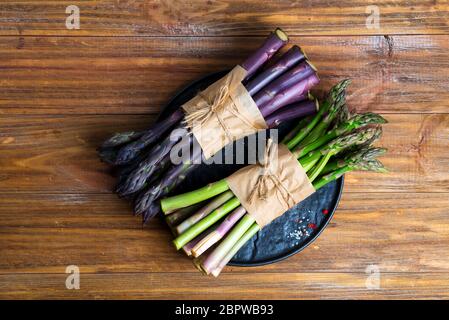 Fresco naturale biologico due fasci di verdure di asparagi verdi e viola su sfondo ligneo. Foto Stock