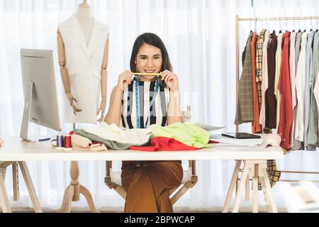 Ritratto di giovane donna asiatica designer che lavora e scegliendo abiti multicolore sul posto di lavoro, startup di piccole imprese, imprenditore proprietario di affari, moder Foto Stock